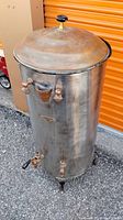 Full view of copper still showing front with three valves, copper lid with black knob, silver patina on surface.