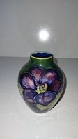 Front side view of the small pottery vase with green glaze and large purple flower design.