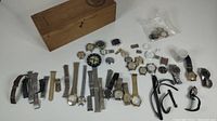 Overview of wooden box and scattered watch parts, bands and heads on white surface