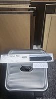 Photo shows a sealed white labeled box containing a black stylus pen. Includes a metallic silver carrying case with a handle hole and a folded instruction manual.