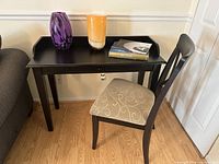 Photo showing a decorative purple and black vase, an orange and white vase, and a hardcover book titled 'Picturesque Rome' arranged on a black desk with a chair nearby.