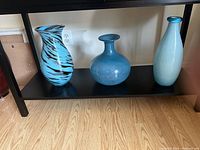 Photo of three blue vases on a shelf showing different shapes, heights, and finishes.