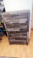 Front view of the grey dresser showing the five drawers with black metal handles and wood plank design.