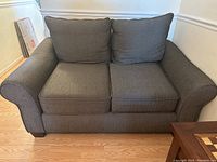 Front angled view of the gray fabric loveseat showing two seat cushions and two back cushions with armrests and wooden legs.
