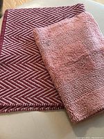 Top view of two bath mats: a red herringbone patterned rug and a smaller pink plush bath mat.