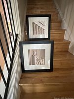 Two black framed square art prints with glass showing Lincoln statue and architectural columns, leaning on stair steps.