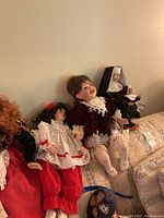Wide view of four collector dolls seated on a couch including porcelain and plastic dolls dressed in various detailed outfits.