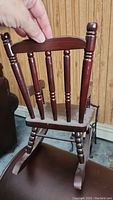 Wood doll rocking chair held by hand showing spindle backrest and rocking base