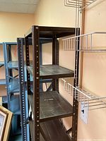 Photo of brown metal shelving unit with six shelves positioned against a wall next to similar shelving units and some wire racks.