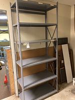 Full view of the assembled metal shelving unit showing five metal shelves and vertical perforated supports.