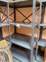 Photo showing metal shelving unit with four flat shelves, light gray steel construction with perforated support beams.