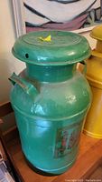 Green milk can showing overall shape, lid with yellow paint spot on top, and faded decal on side