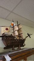 Side view of wooden model ship showing sails with red crosses and Irish flag on main mast.