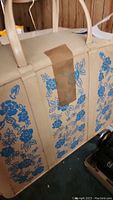 Slip-over plastic case for the sewing machine, beige with blue floral design and handles, taped in center.