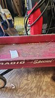 Side view of wagon showing 'Radio Special' branding, red metal body with rust and dirt, wood floor background.