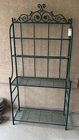 Front view of green baker's rack with decorative spiral detail and three wire shelves.
