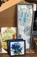 Five pieces of framed wall art visible stacked and grouped together including two blue floral square frames, one large rectangular blue mosaic floral frame, and the 'Vacanze in Italia' piece with corner packaging visible.