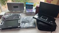 Photo showing three personal DVD players, one with a car mount, Sony CD player stereo, and several DVD-RW discs on a window sill.