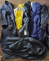 Five women’s coats displayed side-by-side on wood floor, including dark gray wool dress coat, bright yellow Columbia winter jacket, black leather coat, navy blue parka, and darker leather jacket.