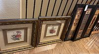 Full set of five framed wall art prints including two floral prints and three geometric/tribal prints leaning against stair railing on wood flooring.