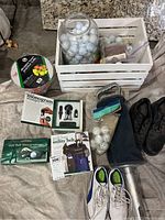 Photo showing the entire lot including golf balls in crate, golf shoes, monogram stamper set, utility belt package, and practice ball bucket.