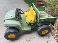 Side view of green and yellow John Deere Gator kids ride-on tractor showing seats, tires, and cargo bed.