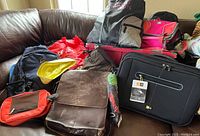 Lot of bags on a couch including backpacks, purses, and a brown leather bag.