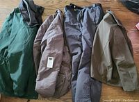 View of four men's winter outerwear items including jackets and a dress coat arranged side by side on a wooden floor.