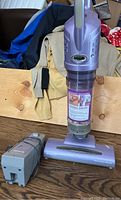 Shark Cordless Stik Vac vacuum and battery charger displayed upright on wooden surface with cloth background.