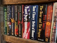 Shelf showing hardcover books by Steve Berry, Douglas Adams, Tom Clancy, and William Dietrich