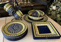 Photo of stoneware mugs on wooden mug rack, stacked plates, and square plates showing pattern and colors.