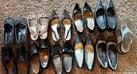Photo showing 12 pairs of women's shoes and heels arranged on carpet. Varied styles including heels and flats in neutral colors.