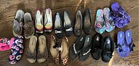 Top-down view of 11 pairs of women's shoes arranged on wooden floor showing a variety of styles and colors.