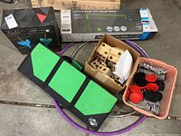 Overview of all items in the lot including boxed volleyball net, yard dice, dart set box, checkers game pieces in container, and green-black game case bag on floor.
