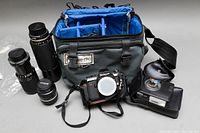 Photo of Nikon N2000 camera, Nikon lenses including 55mm, Tamron 80-210mm, Nikon 100-300mm lenses, Nikon Speedlight SB-15 flash, Lowe-Pro bag and accessories laid out on a surface