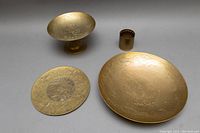 Overview of four brassware items on a gray surface showing their size and etched designs