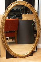 Full view of the large oval mirror showing the ornate gold carved frame