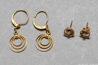 Pair of 10K gold circular drop earrings and 10K gold diamond stud earrings displayed side by side on gray surface