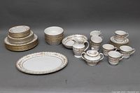 Full set arranged showing all items in lot including plates, bowls, creamer, sugar bowl, teacups, and saucers with floral gold design.