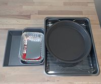 Top-down view of assorted baking trays and foil pans stacked on a wooden table.