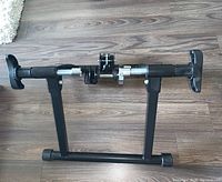 Full view of the foldable black metal bike trainer stand placed on wooden floor.