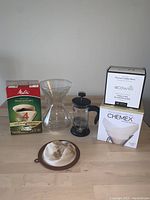 Photo showing Chemex coffee maker, French press, Melitta coffee filters, Ecowilli coffee filters, and a reusable cloth filter arranged on a wooden surface.