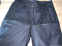 Front view of men's black Columbia ski pants showing zipper pockets and snap button waistband closure