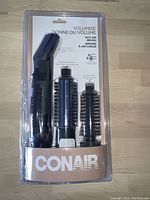 Front view of Conair Volumize hot air brush set in packaging, showing main handle and two brush attachments.