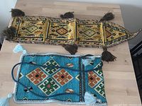 Two handwoven kilim pieces on table: one wall hanging with tassels, one small bag with shoulder strap.