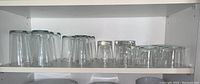 Clear glass drinking glasses on white shelves, three sets with differing shapes and sizes