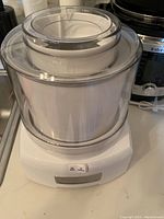 Front upper view of Cuisinart ice cream maker with clear lid and white plastic base with on/off switch.