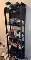 Full view of black self-standing four tier shelf unit with assorted items on each shelf, showing condition and structure.