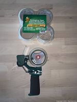 Top view of packaging tape dispenser alongside 3 rolls of packaging tape still in original packaging
