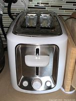 Front view of a white and stainless steel used 2-slice toaster with control knob and buttons.